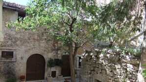 A courtyard with stone walls, a tree, and steps leading to a door. - Superior Apartment (1 person) Residence La Torre (Santo Stefano di Sessanio)