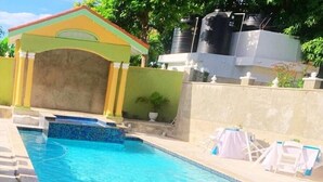 Una piscina rectangular con borde de azulejos, un pequeño área de descanso cubierta y una cerca blanca.