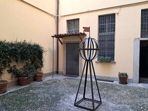A courtyard with a metal sculpture, potted plants, and a building with barred windows. - Studio on two floors in an XVIII century building, just 500m from Duomo Square (Milano)