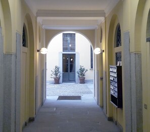 Un couloir doté d’un plafond en arc de cercle, de plantes en pot et d’une porte sur laquelle est apposée une enseigne.