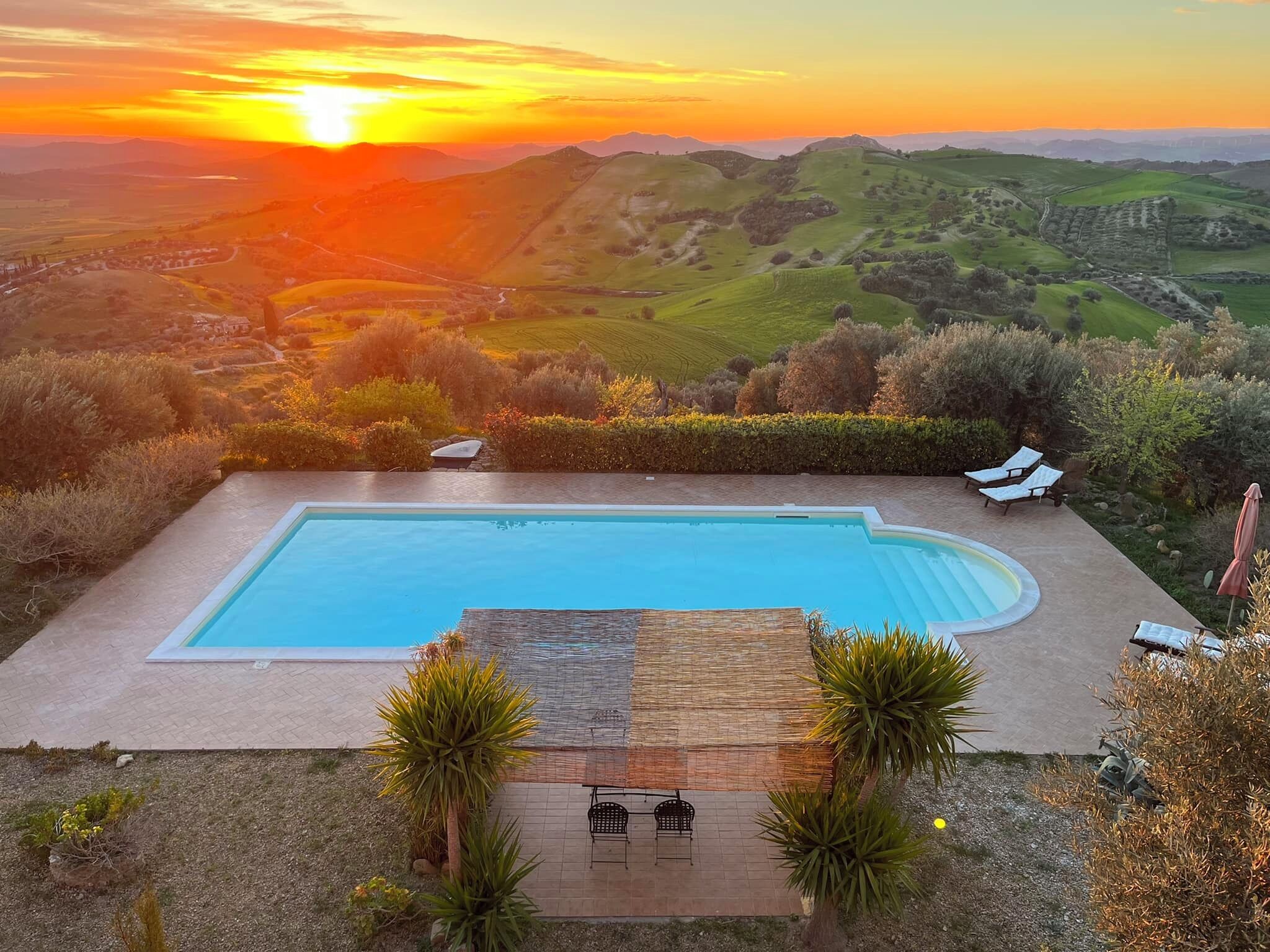 A rectangular swimming pool with a stone deck, surrounded by lounge chairs and a small table.