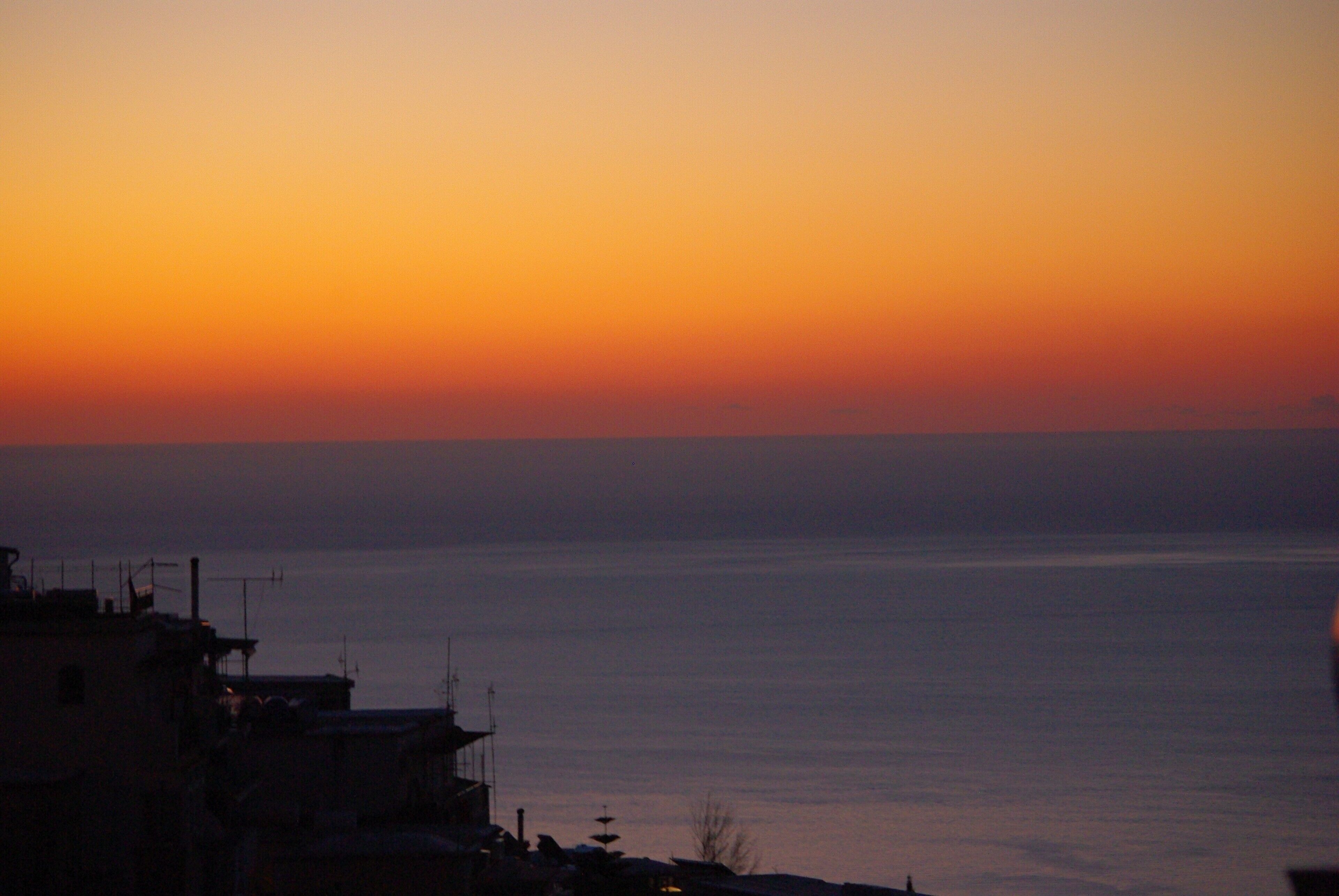 Un atardecer costero con edificios silueteados contra el cielo.