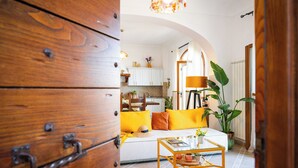 Un salon chaleureux avec un meuble en bois, un canapé blanc agrémenté de coussins jaunes, une table basse et une grande plante.