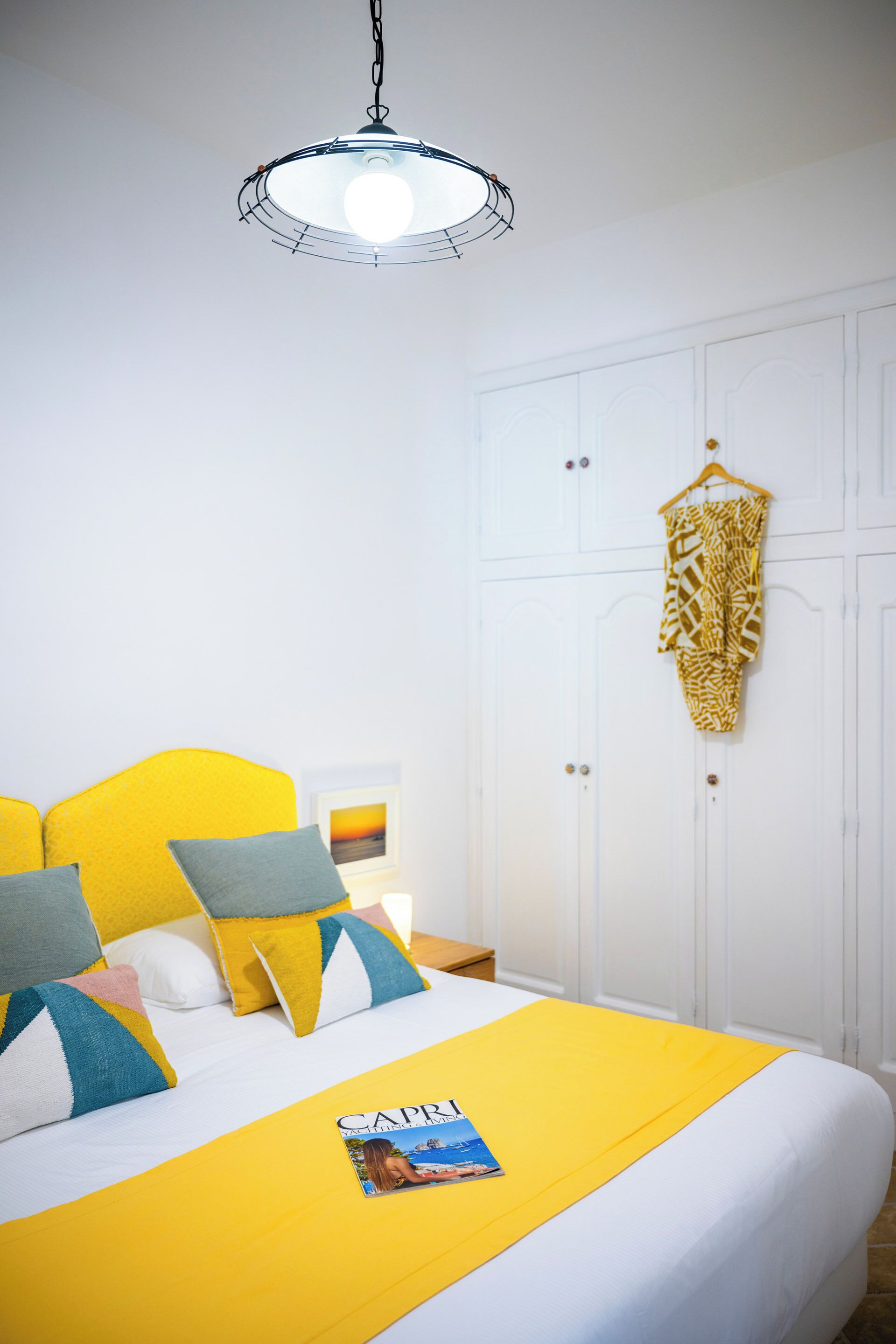 A neatly made bed with a yellow bedspread, a white headboard, and a hanging garment.