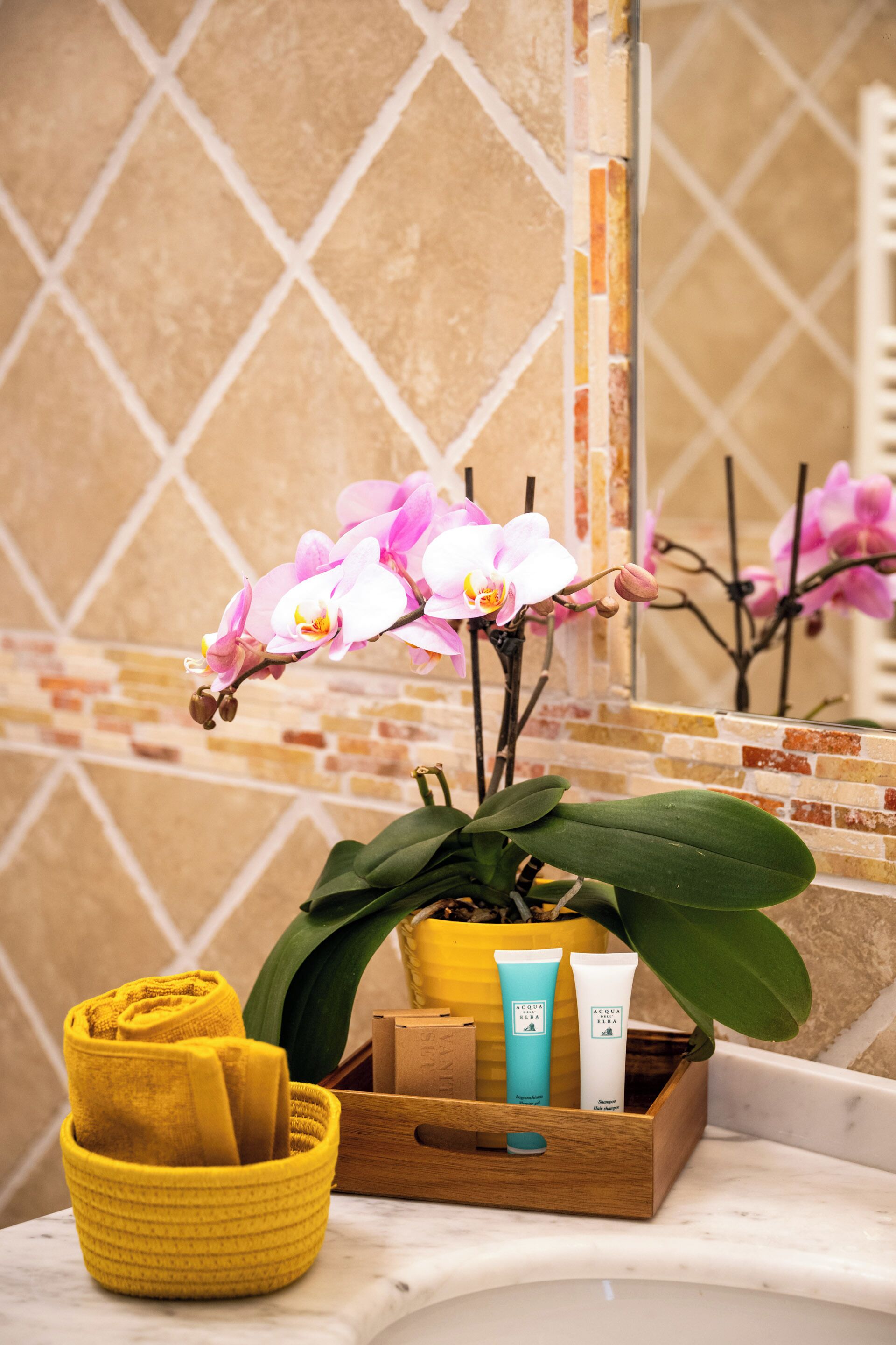 Une salle de bain avec un miroir, une serviette jaune, une orchidée en pot et des articles de toilette.
