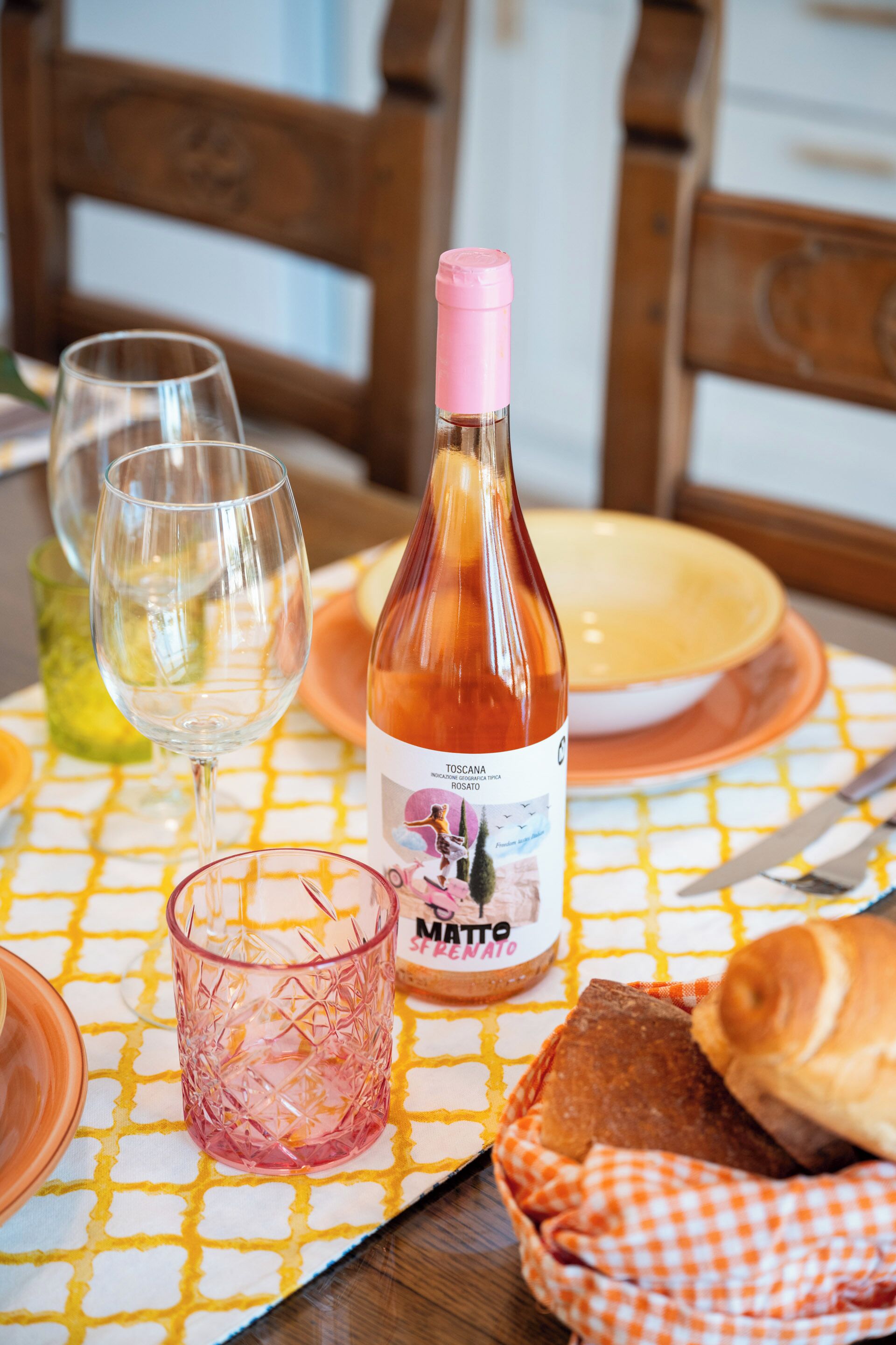 Un tavolo con una bottiglia di vino, bicchieri e un cesto di pane.