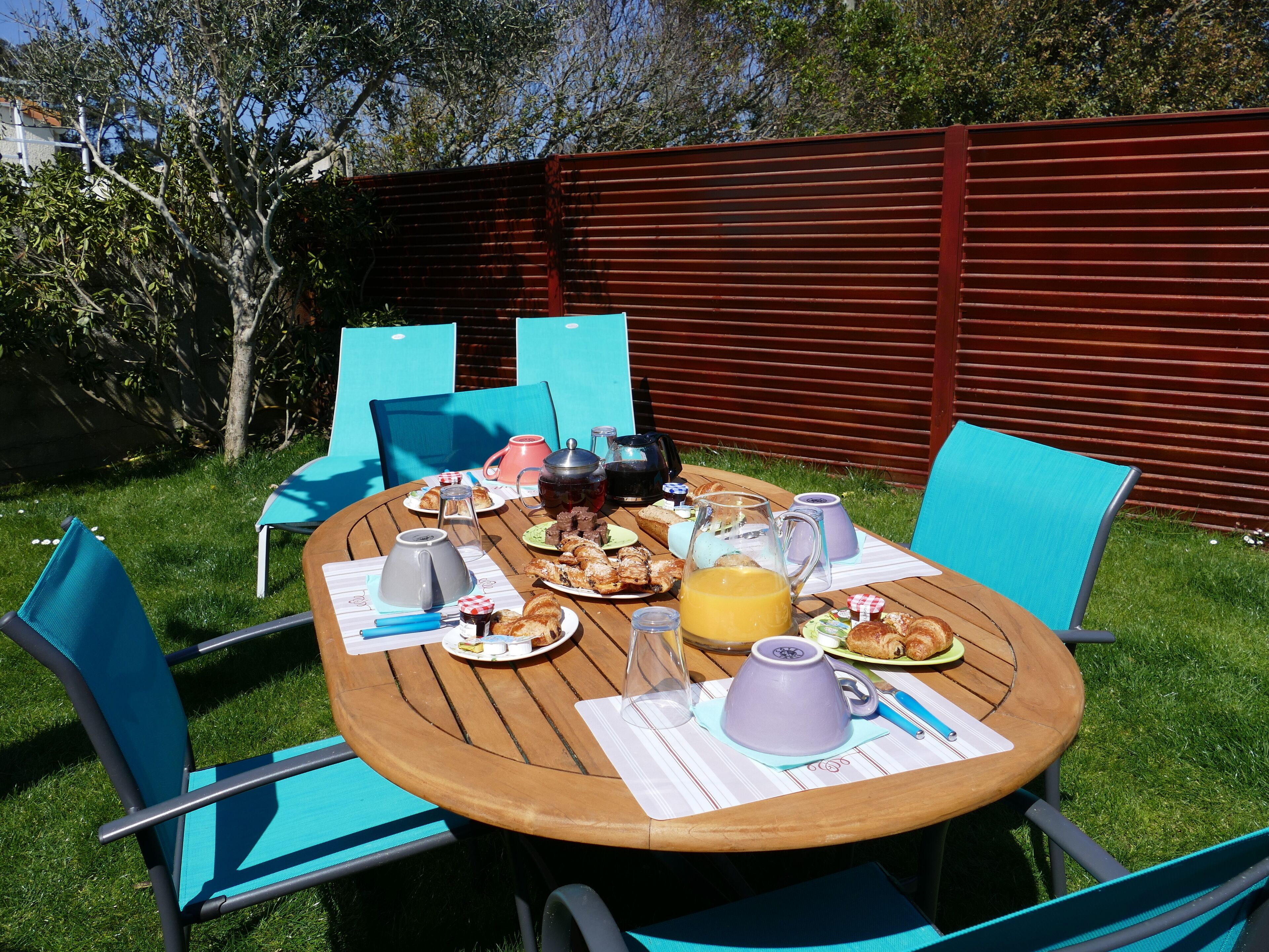 Un espacio exterior para comer con una mesa de madera, sillas azules y diversas opciones de desayuno.