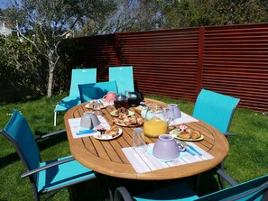 An outdoor dining area with a wooden table, blue chairs, and a variety of breakfast items. - Le Cottage, a house with a garden located 300 meters from the beach (Saint-Palais-Sur-Mer)