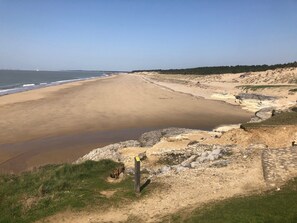 A coastal landscape with a sandy beach, rocky outcrops, and a clear sky.