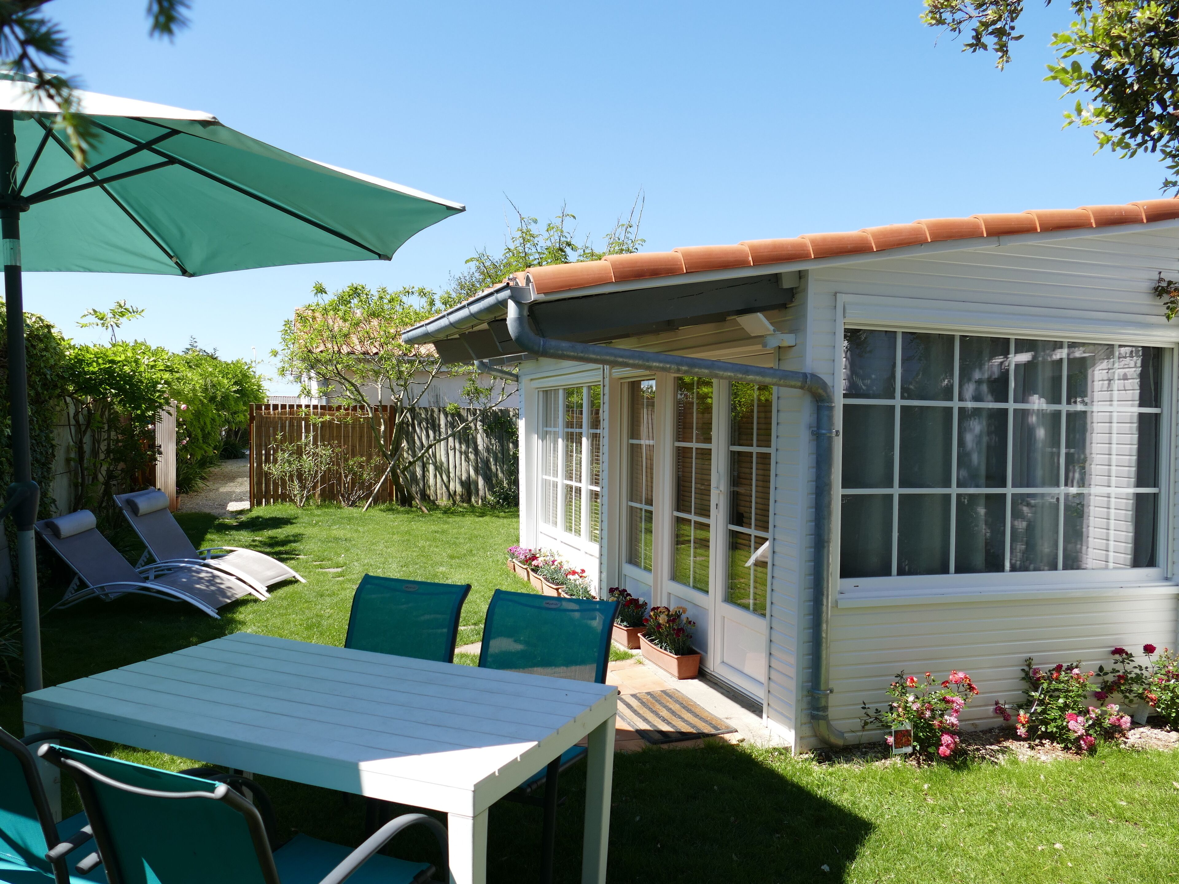 Eine Terrasse mit Tisch und Stühlen, ein überdachter Bereich mit Sonnenschirm und ein kleines Haus mit Fenster.