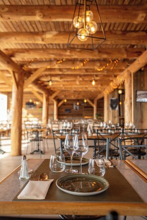 Un interior de madera con mesas dispuestas para comer, que incluyen cristalería transparente y platos.