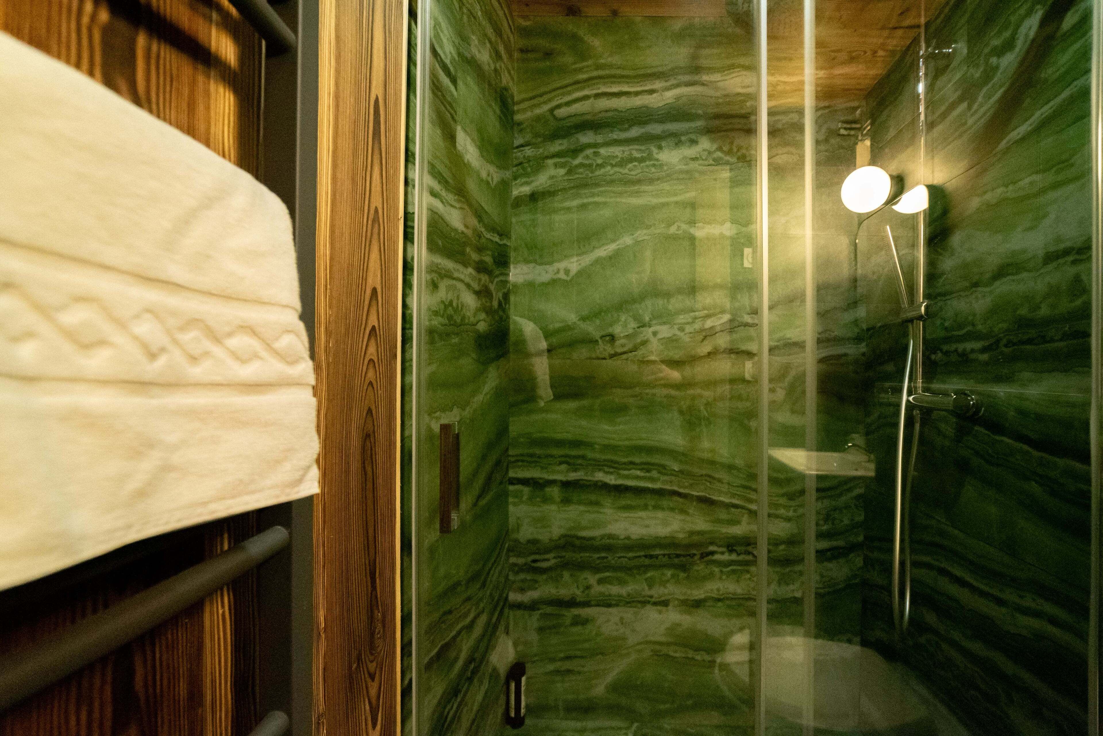 Une salle de bain avec un mur en marbre vert, une douche avec une porte en verre et une serviette blanche posée sur un porte-serviettes.