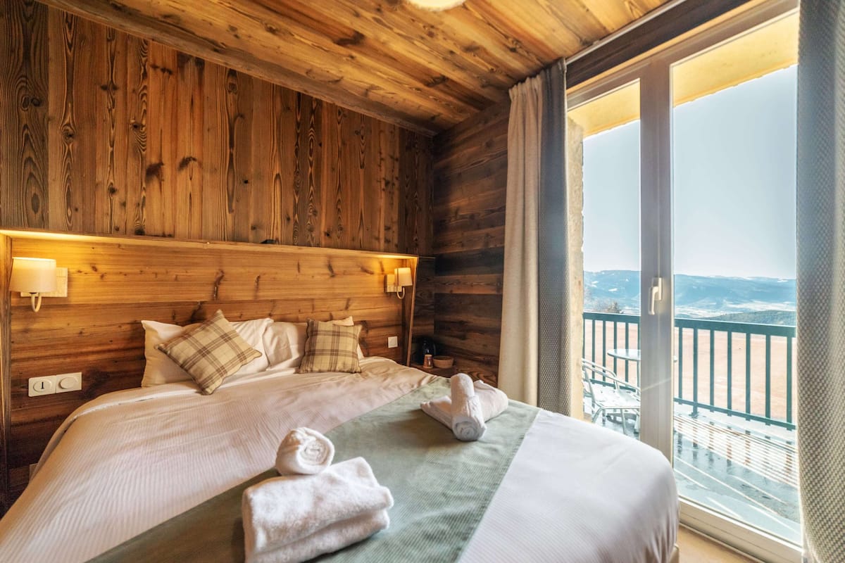 A wooden cabin-style bedroom with a large bed, two bedside lamps, and a view of a balcony with a railing.