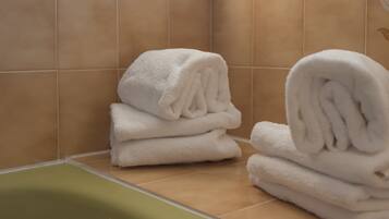 Un baño con baldosas color beige, una bañera verde y toallas blancas apiladas en el suelo.