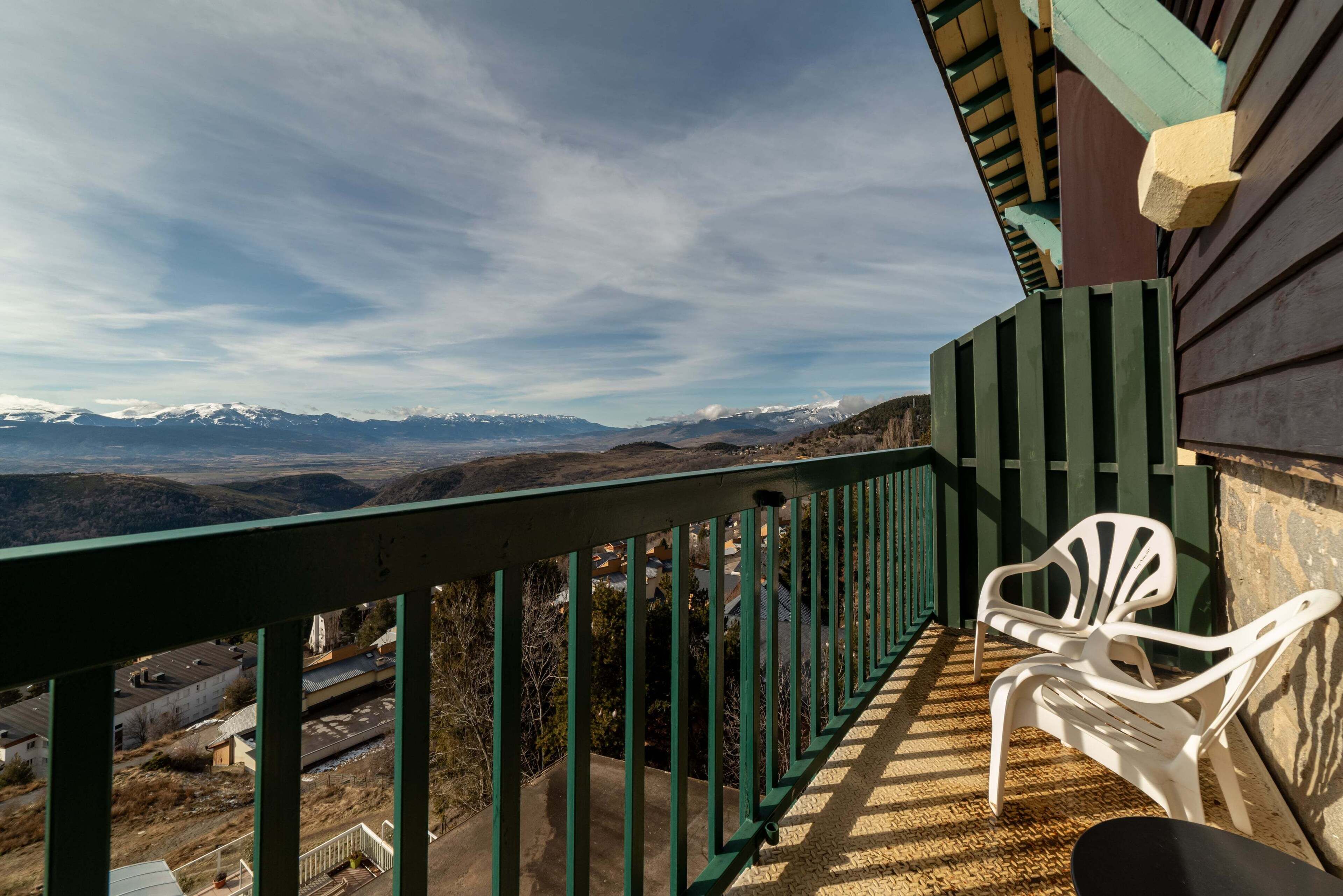 Un balcón con vistas a montañas lejanas, una silla y una barandilla.