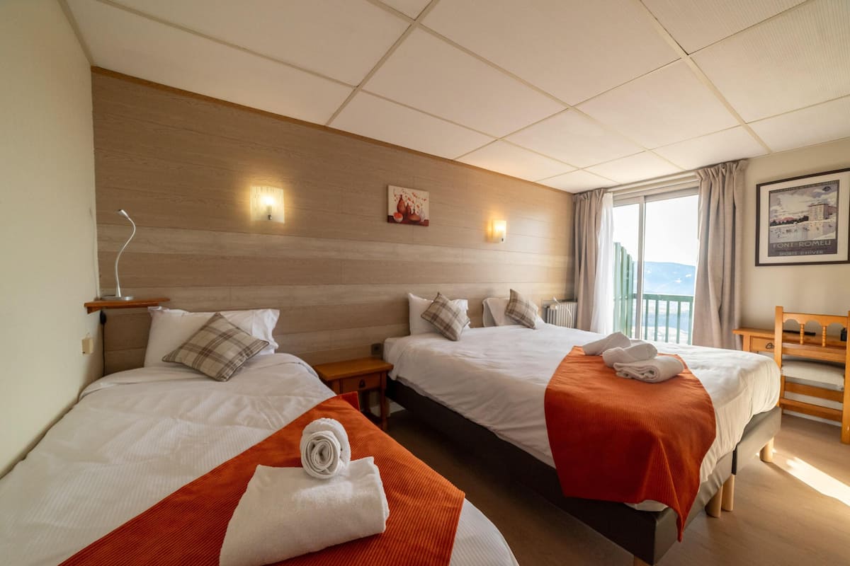 A hotel room with two beds, a wooden headboard, a nightstand, a window with curtains, and a framed picture on the wall.
