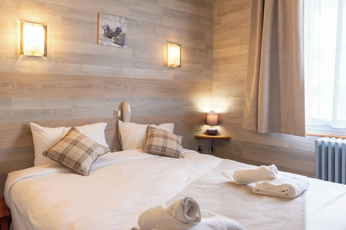 A neatly made bed with pillows, a bedside lamp, and rolled towels on a wooden wall bed.