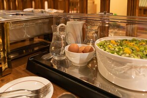 A buffet setup with a tray containing a bowl of eggs, a pitcher of water, and a large bowl of salad.
