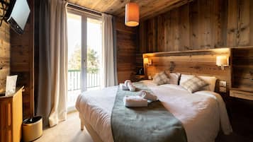 Une chambre de style chalet en bois, dotée d’un grand lit, d’un téléviseur fixé au mur et d’un balcon visible à travers la fenêtre.