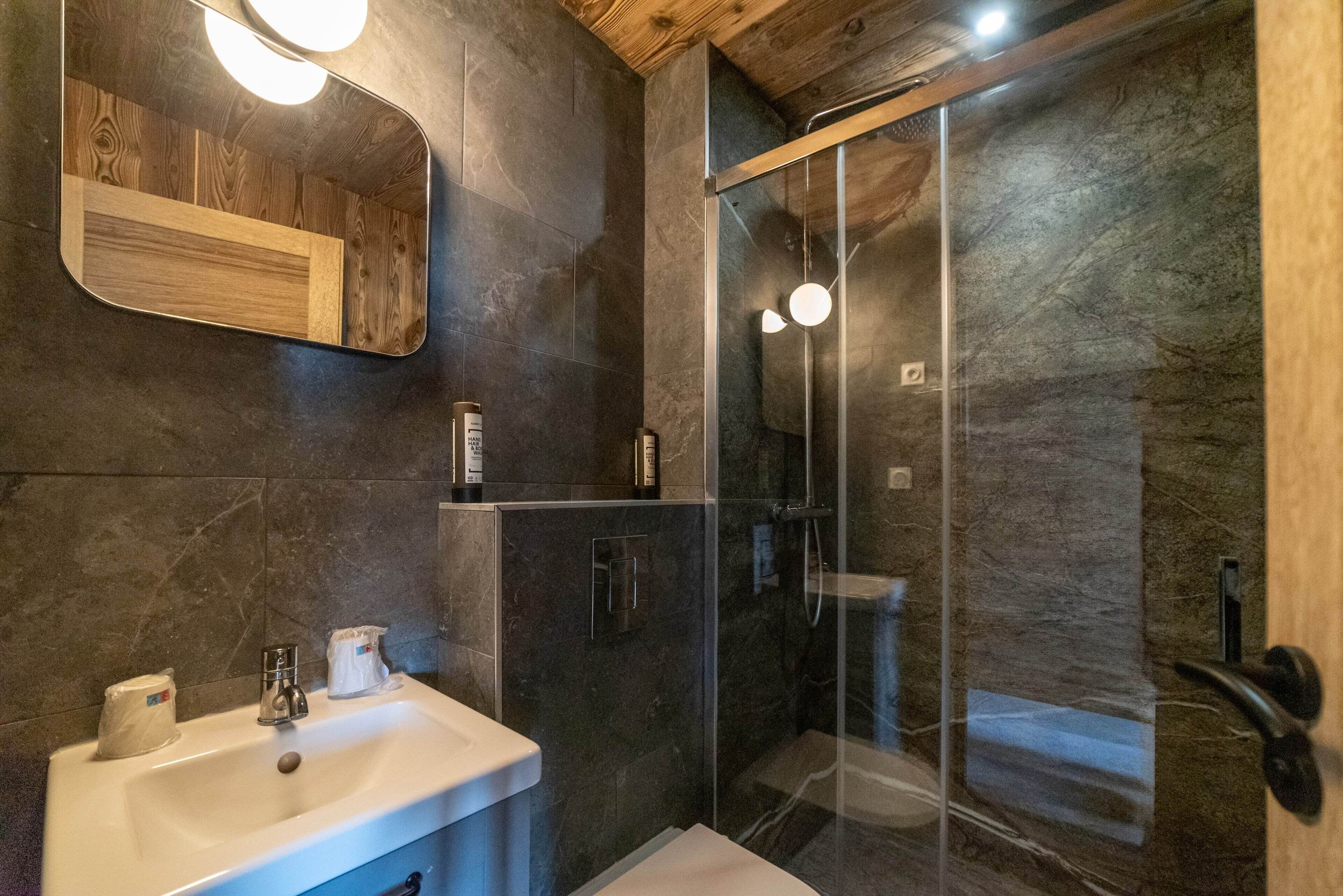 Ein modernes Badezimmer mit einer gläsernen Duschkabine, einem Holztischchen und einem großen Spiegel.