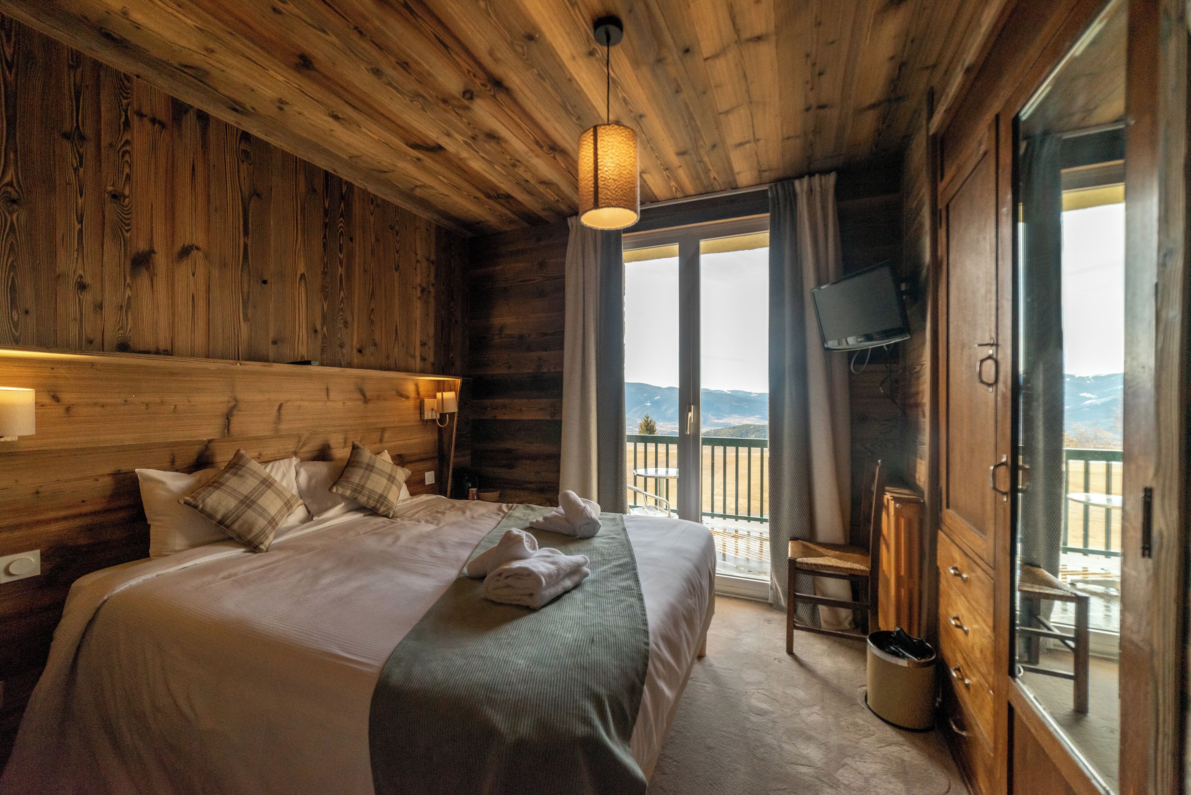Een slaapkamer in een houten chalet, met een groot bed, een televisie en een balkon met uitzicht.