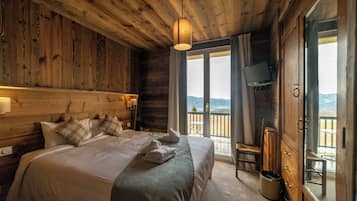 Une chambre dans un chalet en bois, avec un grand lit, une télévision et un balcon offrant une vue panoramique.