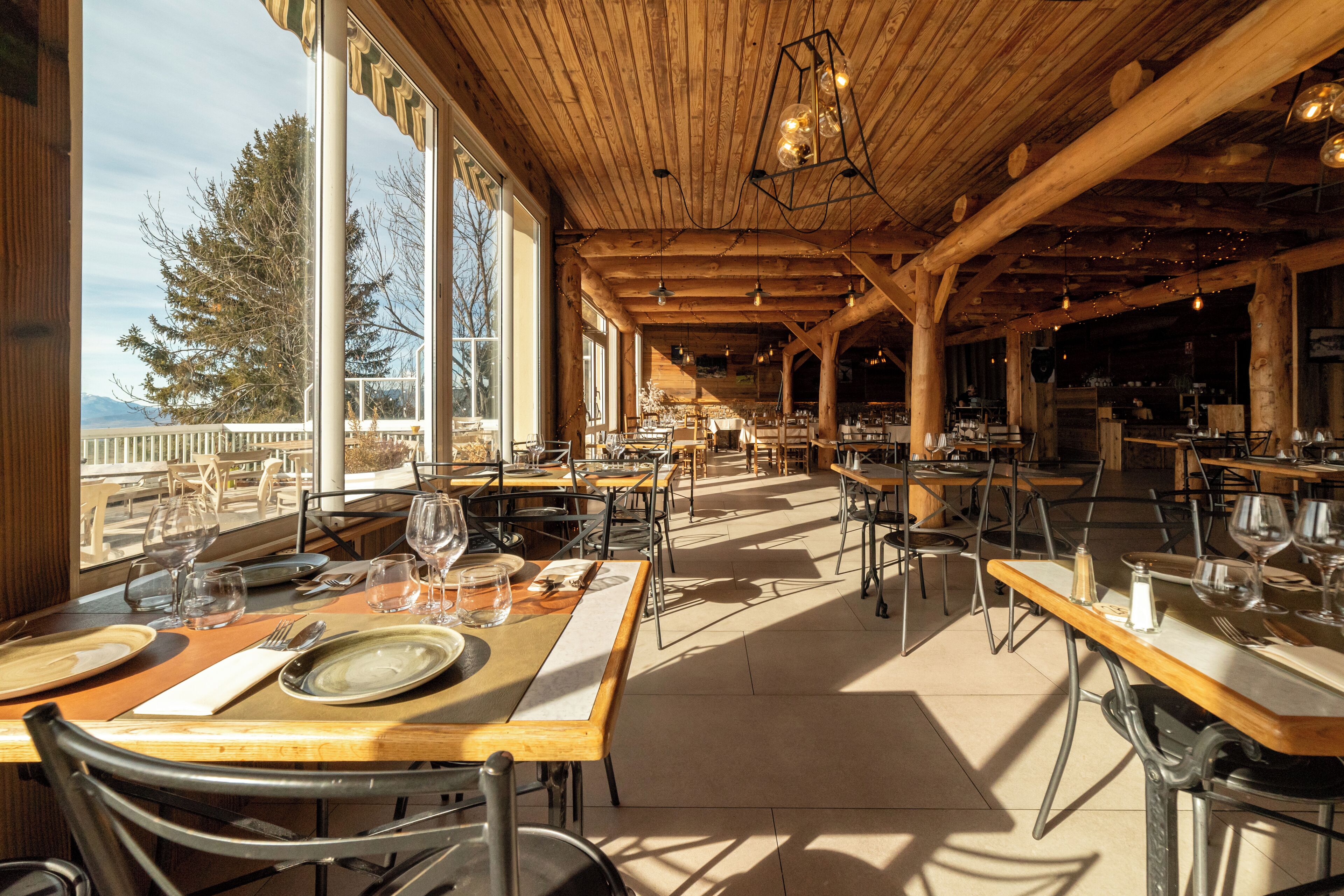 A spacious restaurant with wooden beams, large windows, and tables set for dining.