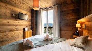 A wooden cabin-style room with a bed, a TV mounted on the wall, and a view of the outdoors through a window.