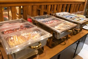 A buffet with multiple food containers including meats, cheeses, and other items.