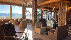 A cozy lounge area with leather chairs and sofas, wooden beams, and large windows offering a view of the mountains. - Hôtel des Pyrénées (Font-Romeu-Odeillo-Via)