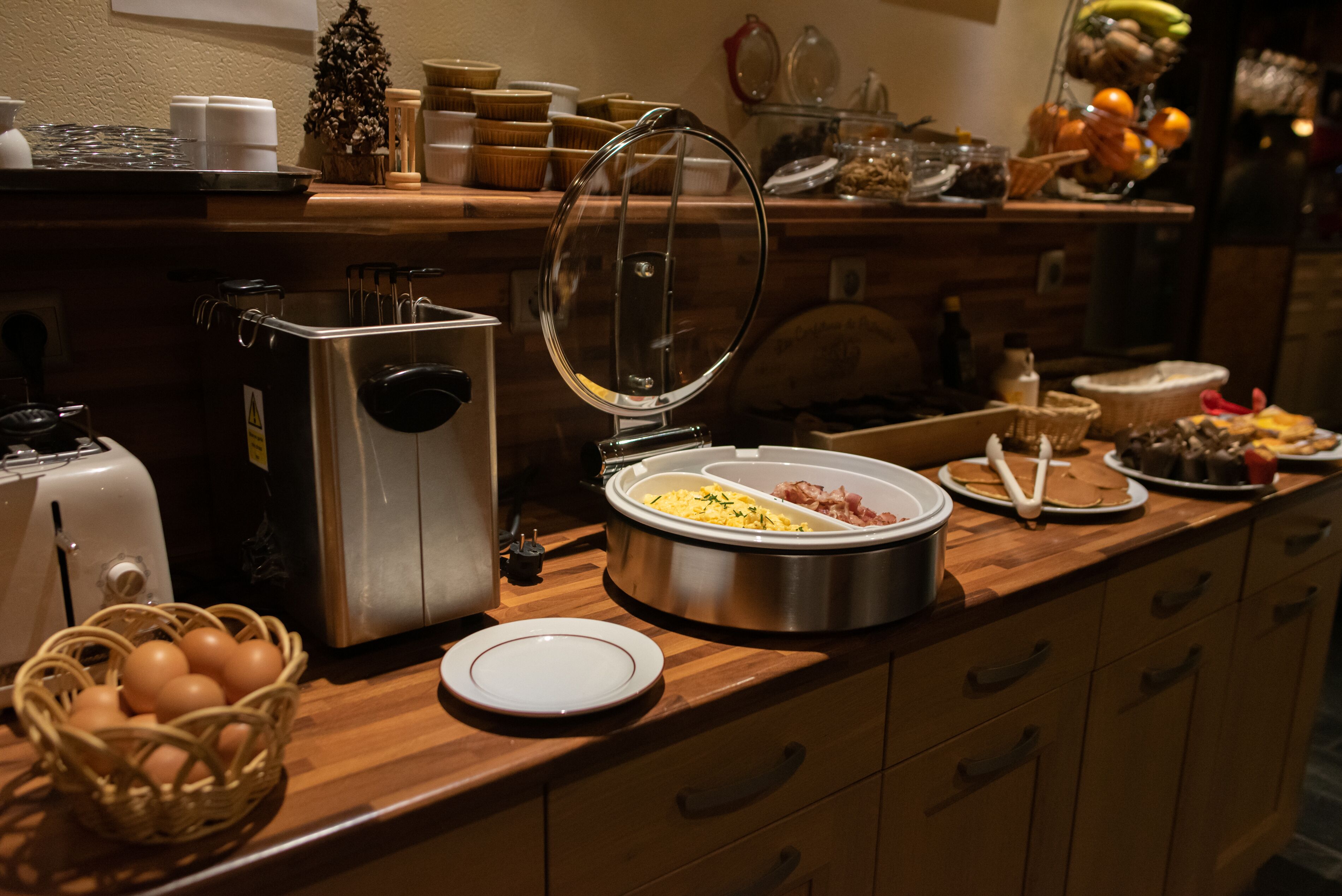 Un buffet proposant divers plats, une machine à café et un panier de fruits.