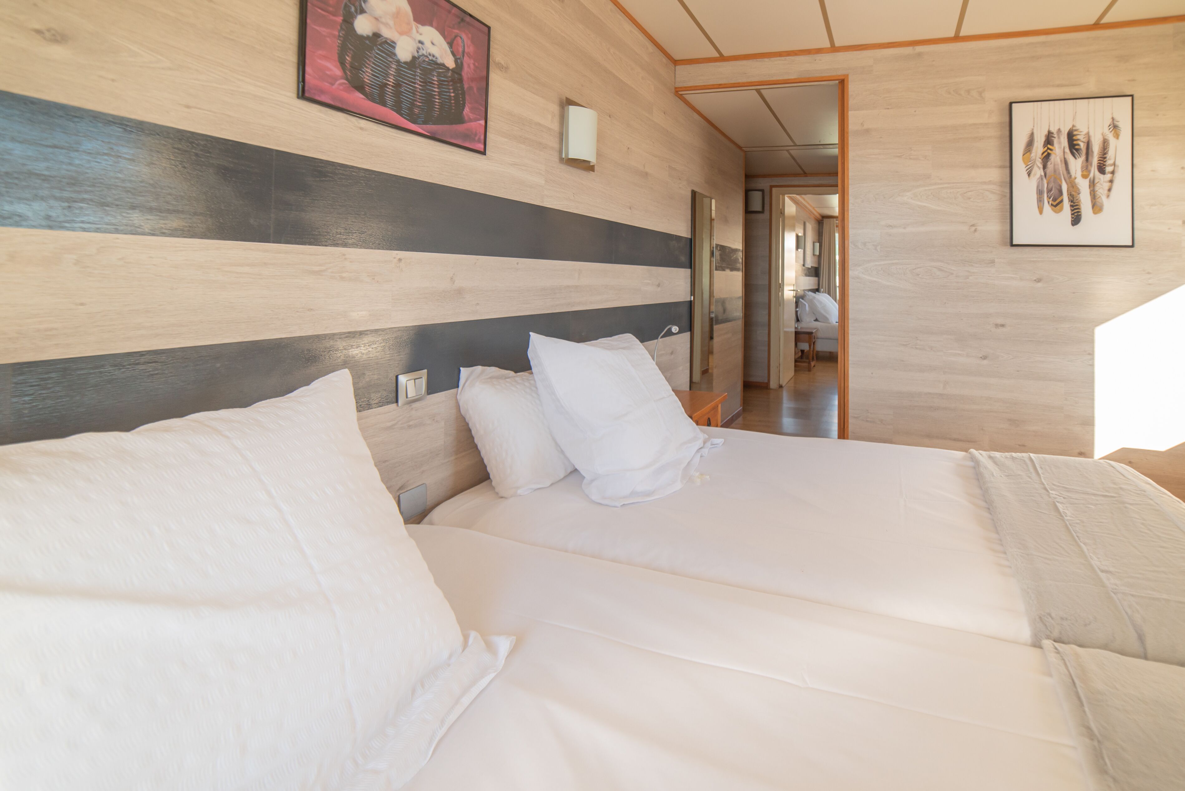 A hotel room with a wooden wall, a bed with white bedding, and a framed picture above the bed.