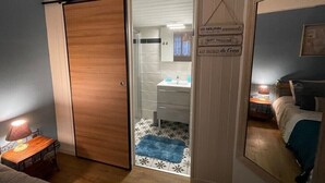 Une chambre à coucher comprenant un lit, une table de chevet, une lampe et une porte coulissante donnant sur une salle de bain équipée d’un lavabo et d’un porte-serviettes.