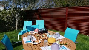 Un espace de restauration en plein air avec une table en bois, des chaises bleues et une variété d’aliments pour le petit-déjeuner.
