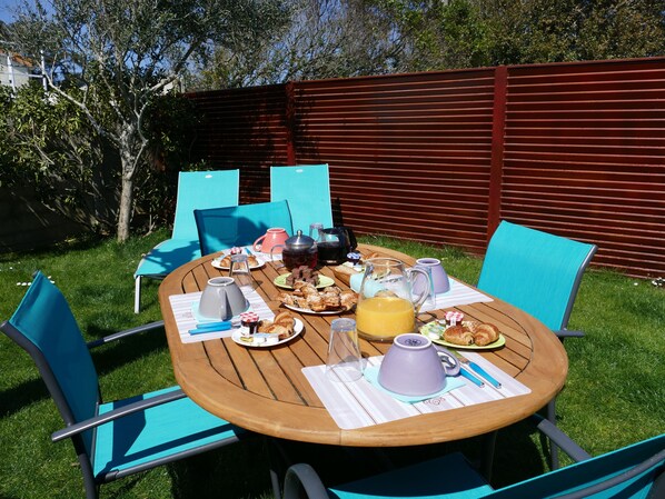 An outdoor dining area with a wooden table, blue chairs, and a variety of breakfast items.