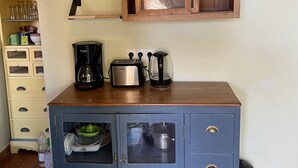 Une cuisine avec un meuble bleu, un meuble en bois au-dessus, et une étagère contenant des ustensiles de cuisine.