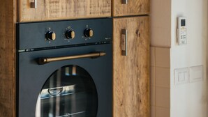 A kitchen with wooden cabinets, a stainless steel oven, and a wall-mounted thermostat.