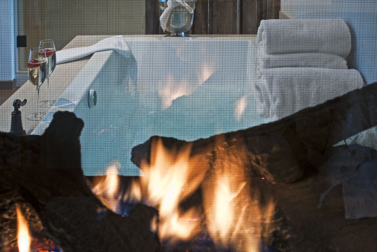 Ein Zimmer mit einer großen Badewanne, zwei Weingläsern und einem Kamin.