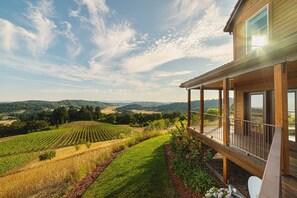 Une maison en bois dotée d’un balcon donnant sur un vignoble et des collines ondoyantes.