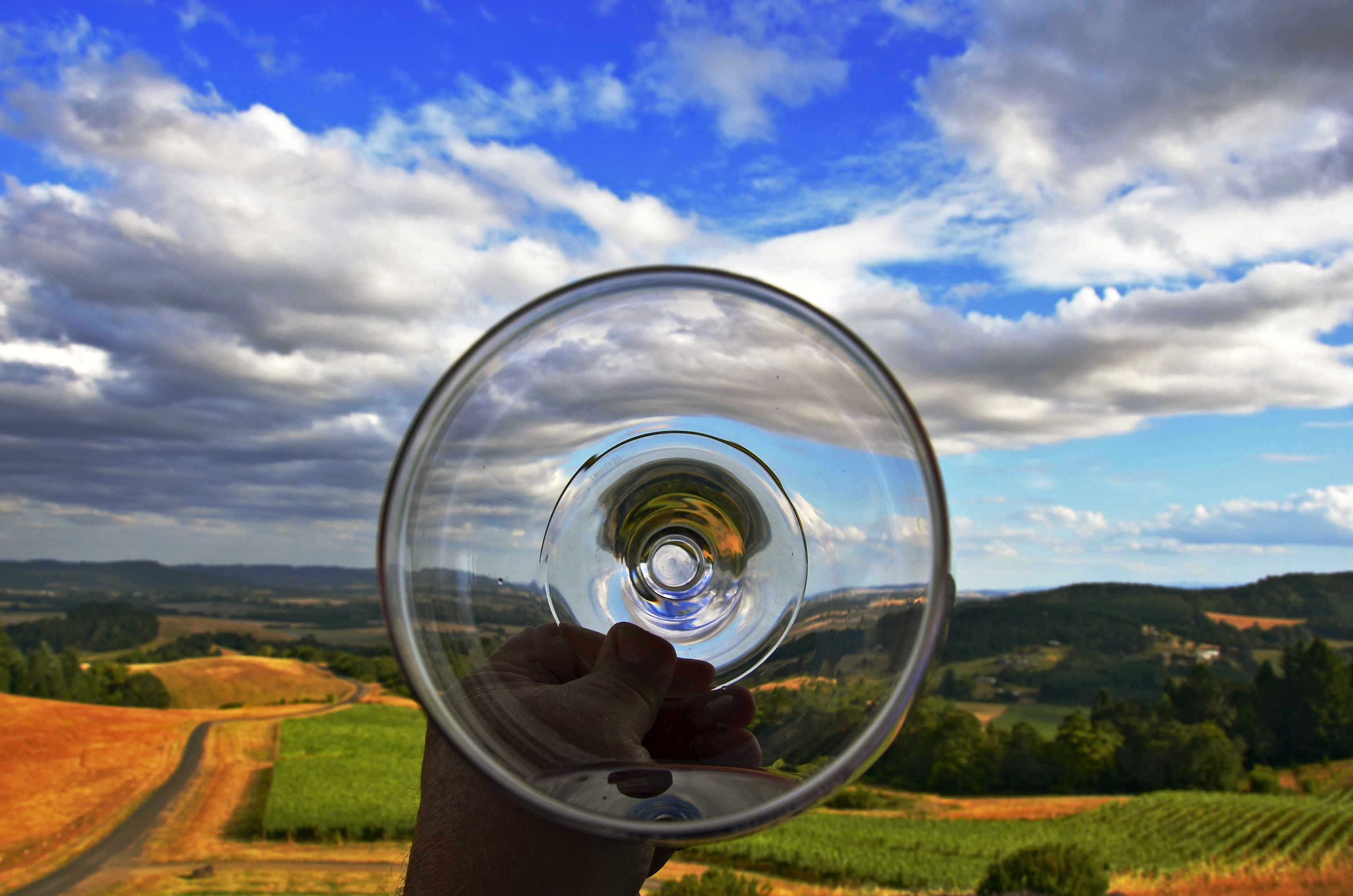 Une main tenant un verre transparent à travers lequel on aperçoit un paysage.