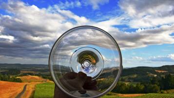 Une main tenant un verre transparent à travers lequel on aperçoit un paysage.
