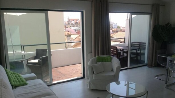 Ein geräumiger Wohnbereich mit einer Schiebeglastür, die auf einen Balkon führt, ein weißes Sofa, ein runder Glastisch und ein Esstisch mit Stühlen.