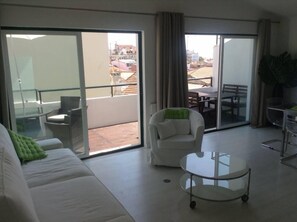 A spacious living area with a sliding glass door leading to a balcony, a white sofa, a round glass coffee table, and a dining table with chairs. - Large terrace, beautiful view in the heart of Lisboa (Lisbonne)