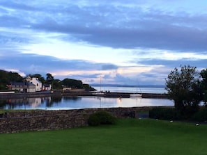A coastal scene with a stone wall, grassy area, and buildings along the shore.
