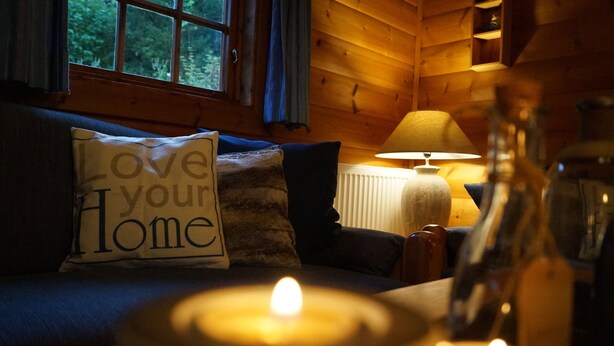 Una habitación acogedora con detalles de madera, una vela encendida sobre una mesa y un cojín con el texto 'Love your Home'.