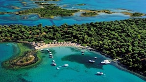 Luftaufnahme einer Küstenlandschaft mit Strand, Booten und dichter Vegetation.