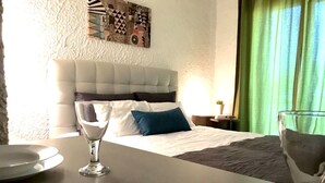 Ein Hotelzimmer mit Bett, Nachttisch mit Lampe, einem Glas Wasser und einem Teller mit Löffel.