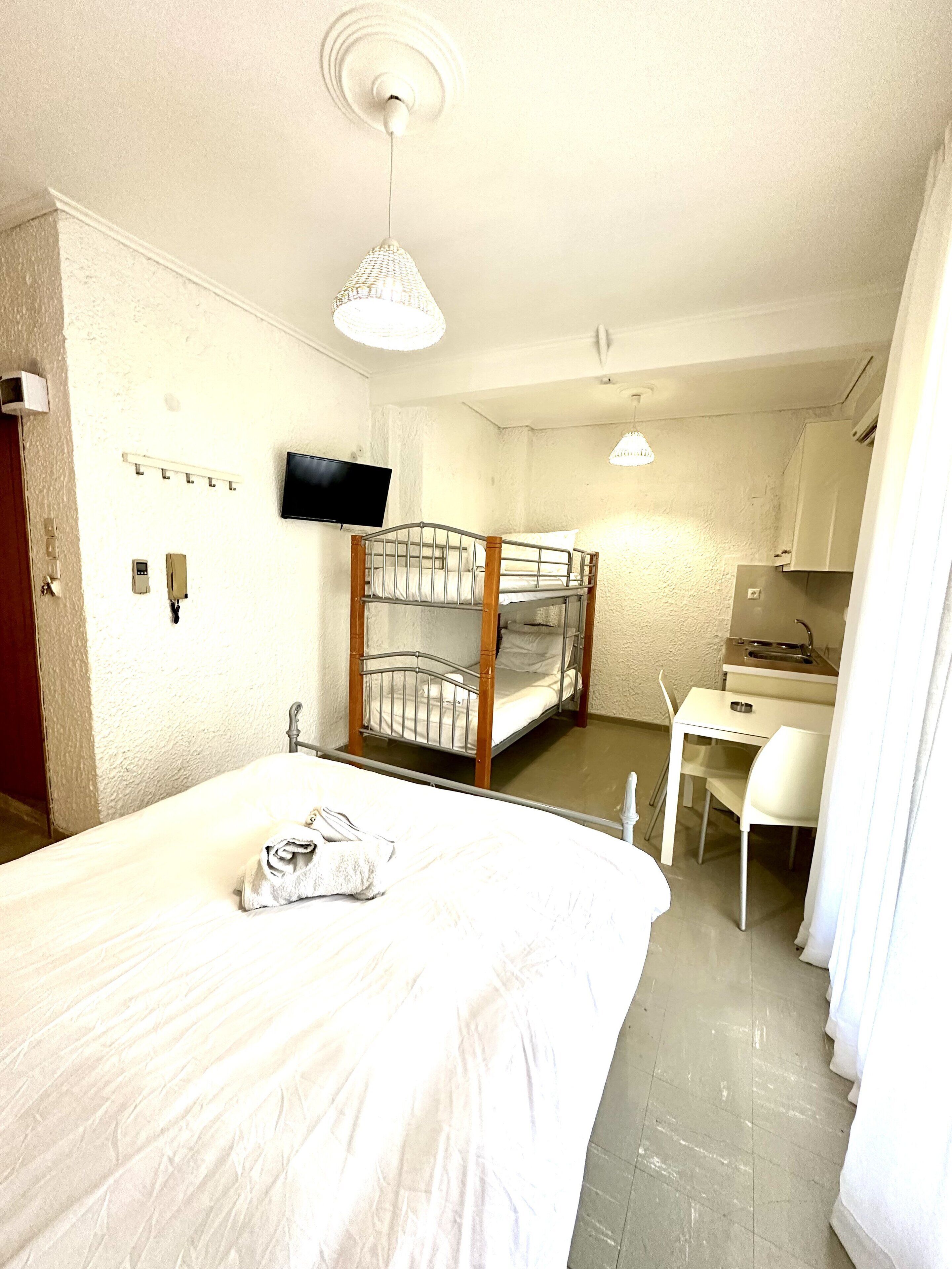 A room with a bunk bed, a desk, a chair, a television, and a small kitchenette.