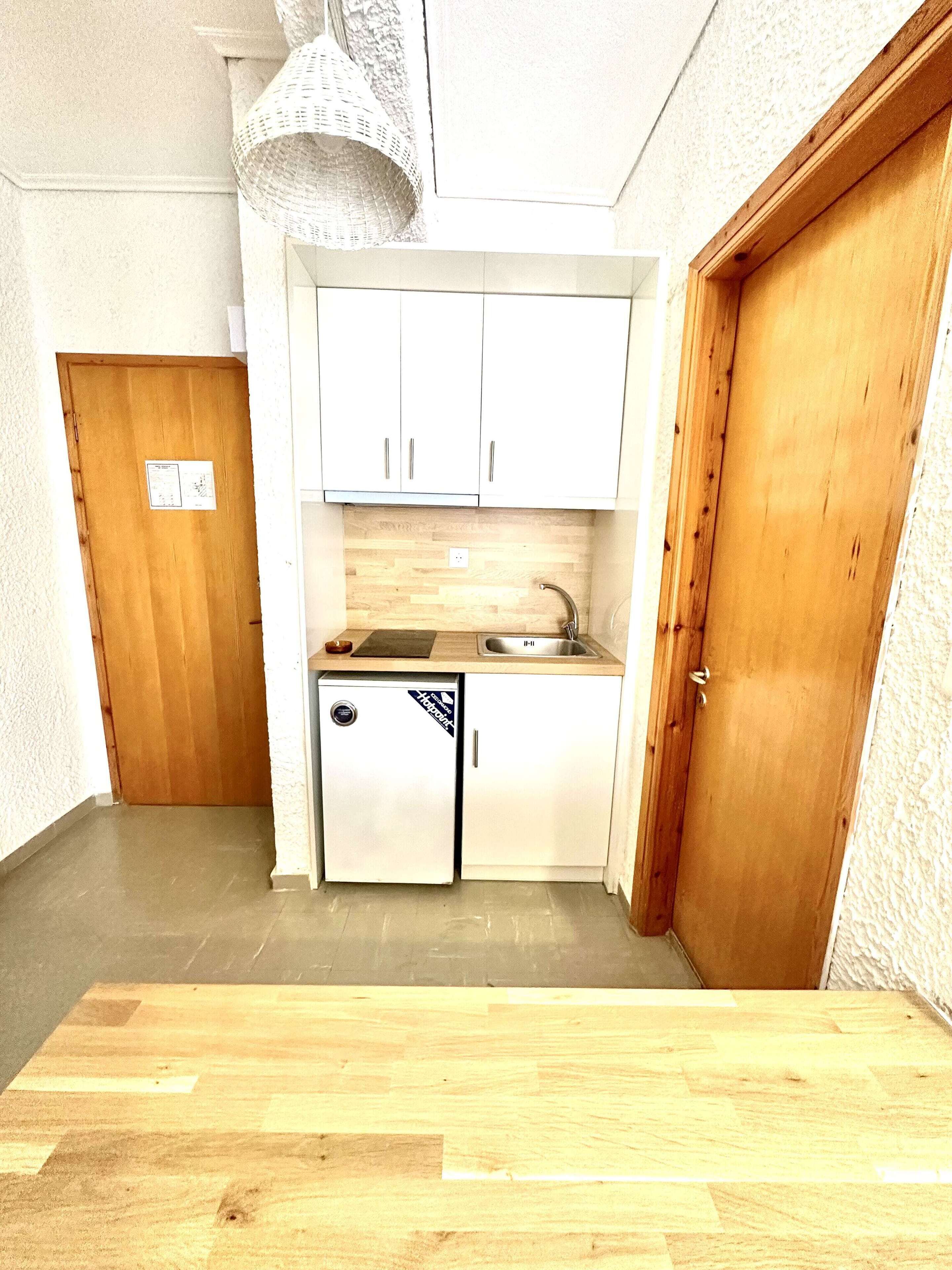 A compact kitchen with white cabinets, a sink, and a small refrigerator.