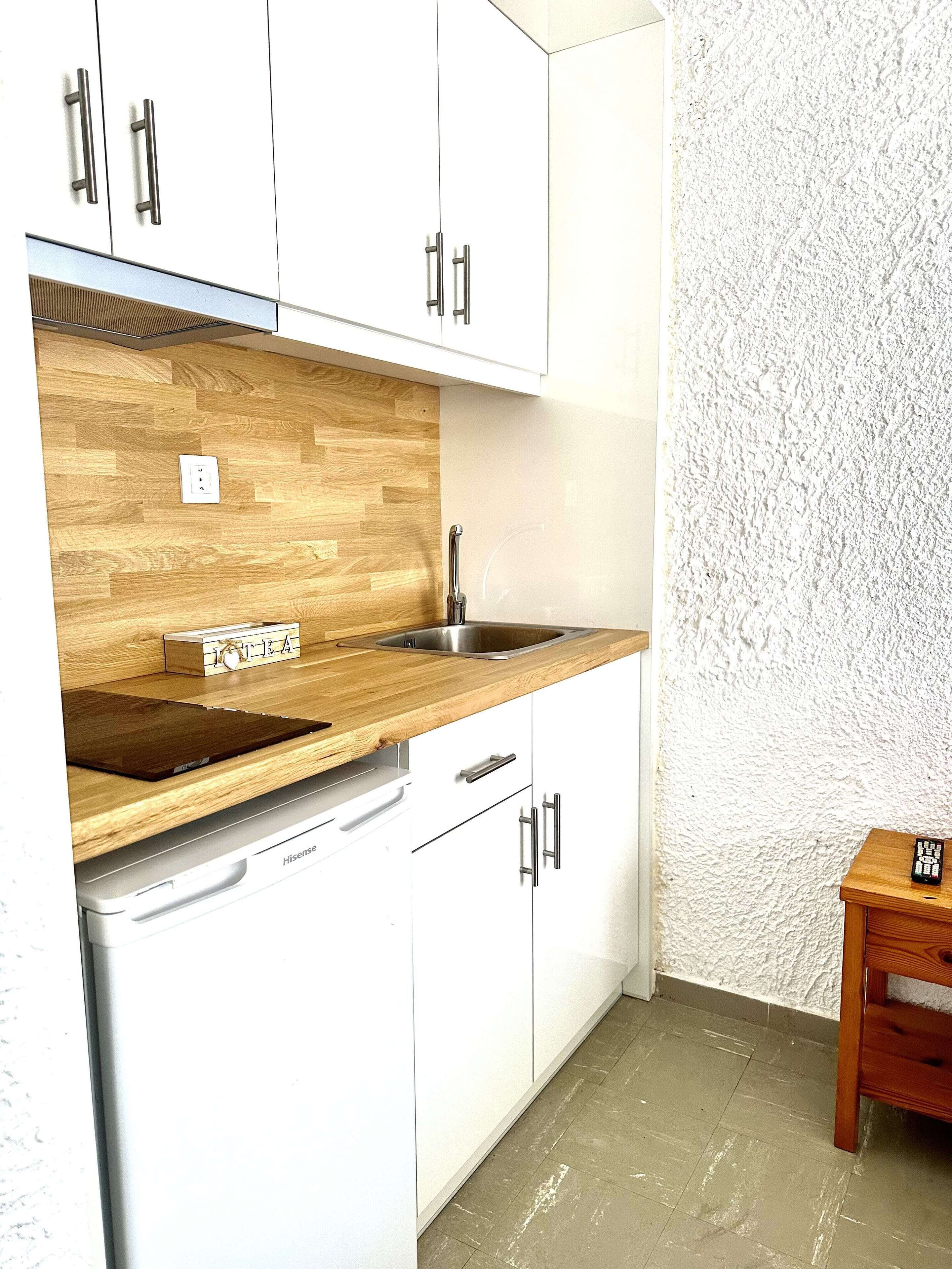 A compact kitchen with white cabinets, a wooden countertop, a stainless steel sink, and a dishwasher.